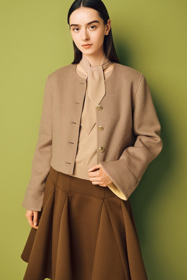 Model is wearing a brown skirt and a beige jacket over a light beige knit top.