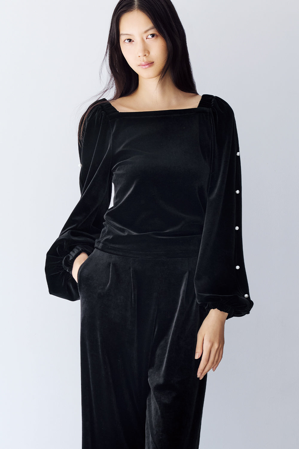 Model is wearing a black velvet top with long sleeves and black pants.