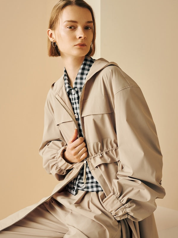 Model is wearing a beige hooded jacket with a drawstring waist.