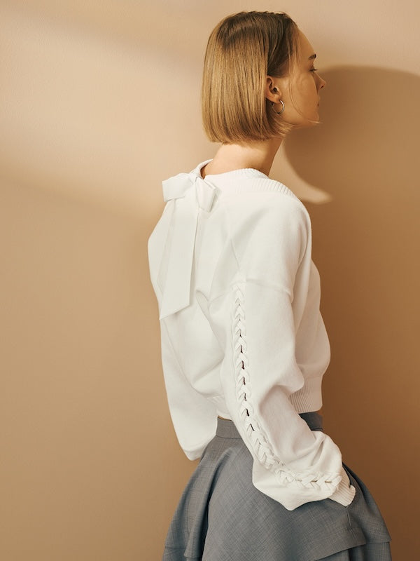 Model is wearing a white knit top with a back bow detail.