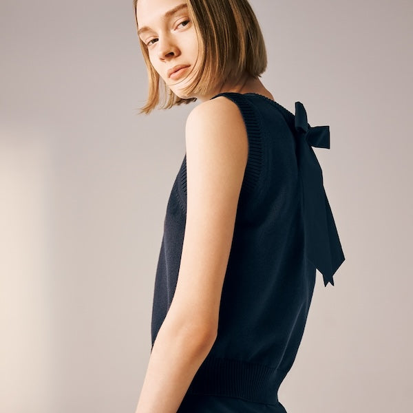 Model is wearing a black sleeveless knit top with a back bow.