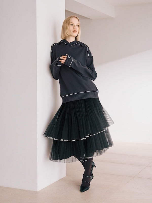 The model is wearing a black top and a black ruffled skirt.