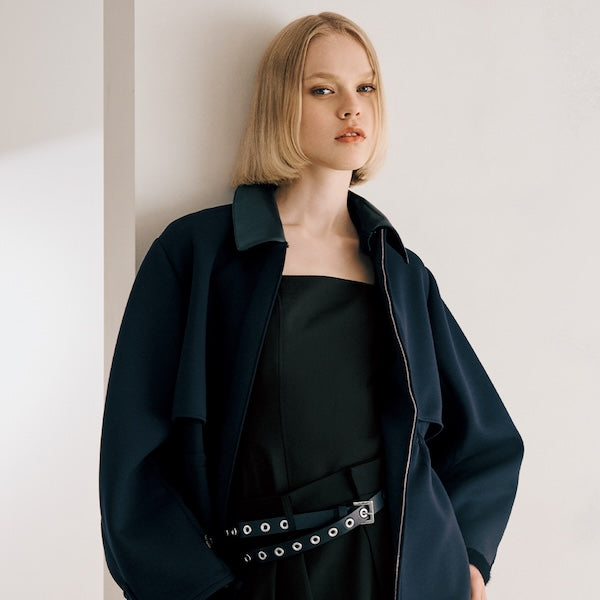 The model is wearing a black jacket, black pants, and a black belt.