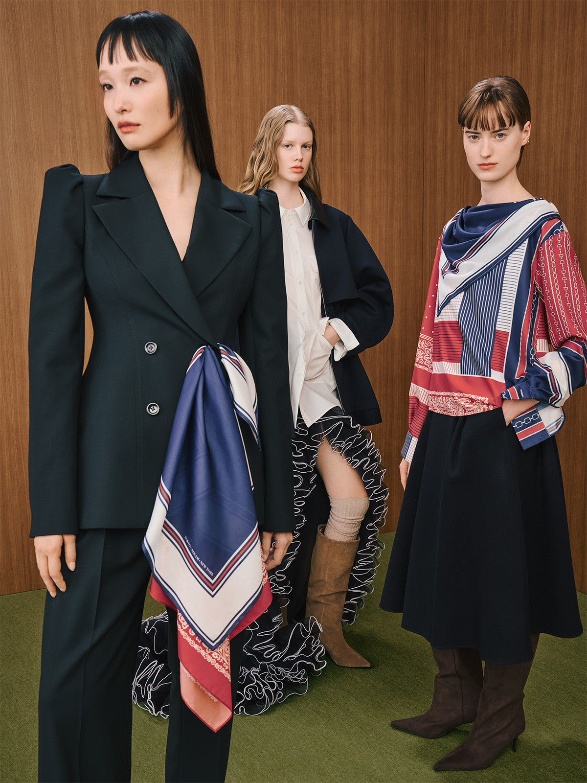 Three models wearing tailored blazers with wide-leg trousers and printed silk scarves.