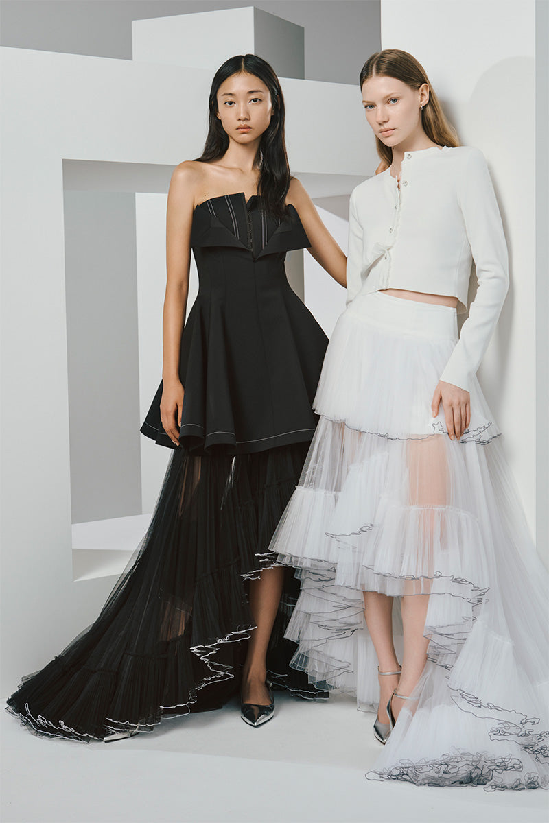 Two models wearing strapless and long-sleeve dresses with layered tulle skirts.